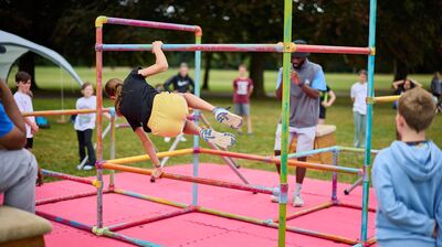 A group of children in a outdoors space, doing Parkour on metal railings.