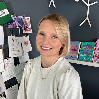 A woman smiling in a gray t shirt, with drawings and stick figures on the wall