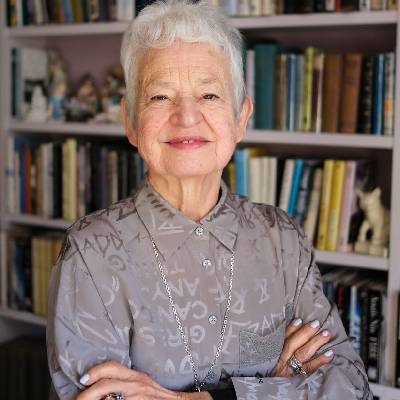 An author stood in front of a book case wearing a grey patterned shirt