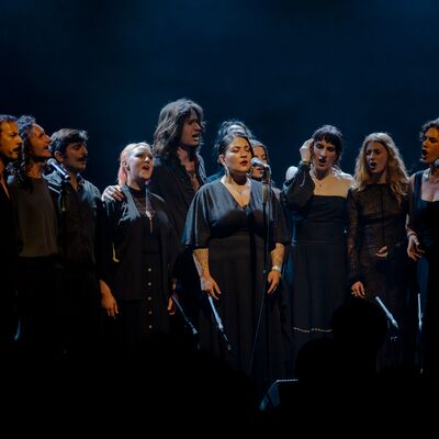 Idrîsî Ensemble singers performing dressed in black on a dark stage