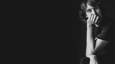 Black and white portrait of a person with short hair resting their face on their hand looking at the camera