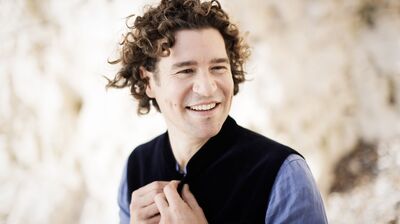 A man with curly hair, smiling wearing a black waistcoat