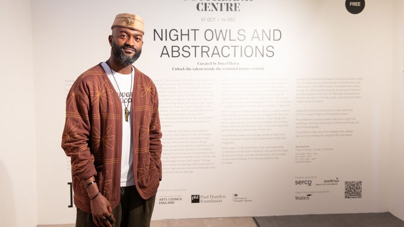 A man in a brown patterned cardigan and embroidered cap stands proudly in front of a Southbank Centre wall text panel for the exhibition NIGHT OWLS AND ABSTRACTIONS.ne. The words 'My Mixtape' have been added in front of him in a large font