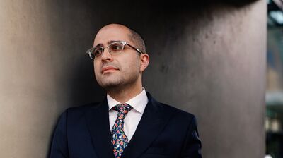 A man wearing a blue suit and flowery tie, leaning against a concrete wall