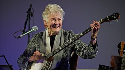 Peggy Seeger onstage with a microphone and a guitar.