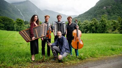 A group of musicians posing in a green valley, with a waterfall in the background