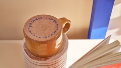 A mug sits upside down with blue writing on the base.