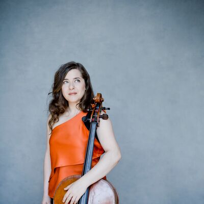 A woman in an orange dress, posing with a cello