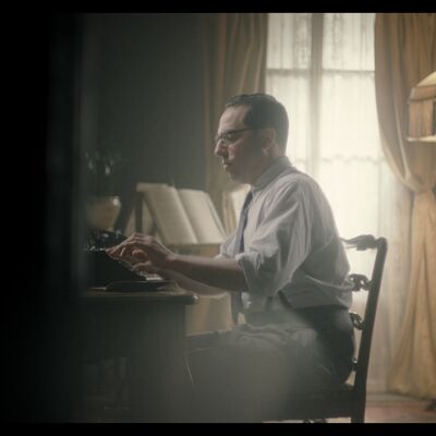 Dan Blaskey portraying polish composer Szymon Laks in the film The Last Musician of Auschwitz; he is glimpsed through an open door seated at table working at a typewriter