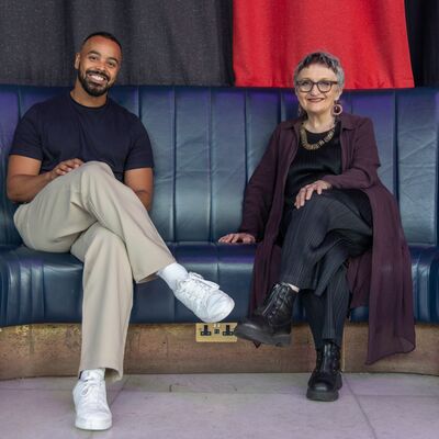 Linton Stephens and Gillian Moore sit side by side on a leather seat in the Southbank Centre's Queen Elizabeth Hall Foyer