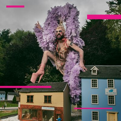 A person wearing a purple feathered headpiece, standing on miniature houses