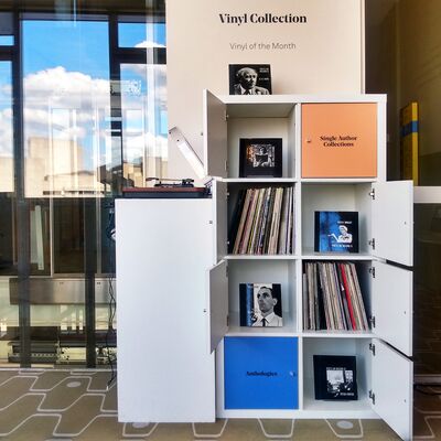 A white shelving unit displaying a vinyl record collection, with some sections holding records and others featuring photographs. The top reads Vinyl Collection Vinyl of the Month.