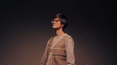 A person holding a trumpet standing with their eyes closed and palms facing up