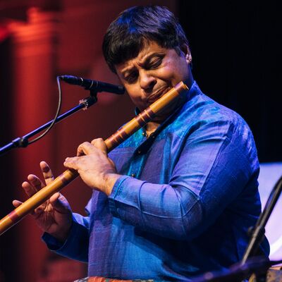 A man wearing a blue shirt playing the bamboo flute into a microphone.