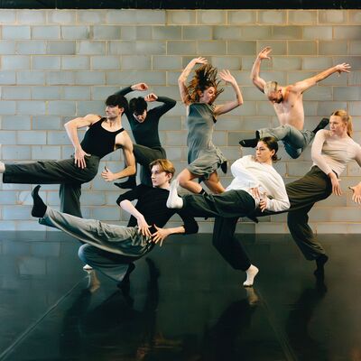 Group of dancers in neutral colours all in different poses in front of a concrete wall