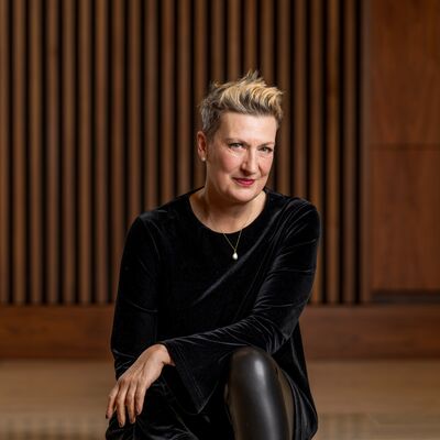 Dame Sarah Connolly dressed in black smiling against a wood panelled wall