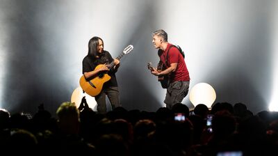 Two musicians stand on stage with guitars and dynamic faces.