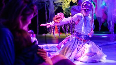 A performer kneeling on the floor, dressed in a metallic outfit and mask