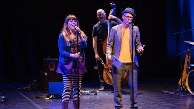 Liv Torc and Chris Redmond stand at mics with jazz band behind them