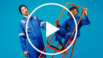 One performer holds an orange ladder, which another performer sits on