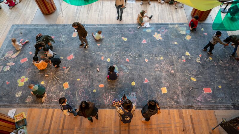 Birds eye view of children drawing on a giant chalkboard.