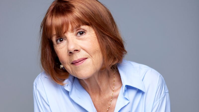 Gisèle Pelicot wearing a light blue shirt, clasping her hands together and smiling slightly