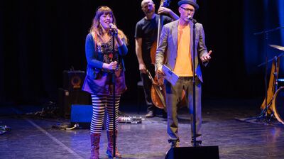 Liv Torc and Chris Redmond stand at mics with jazz band behind them