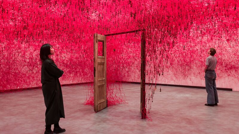 Two people stand on either side of an open door in Chiharu Shiota: Threads of Life