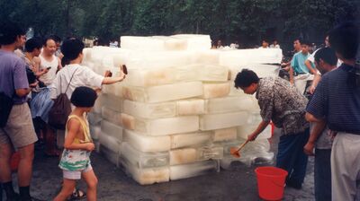 Group of people standing around a large tower of ice blocks, scrubbing them with brushes.