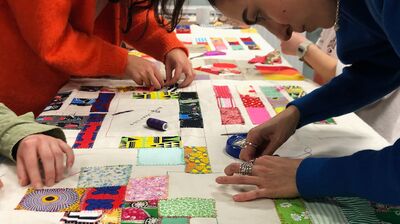 People working on a large fabric patchwork quilt together in a workshop