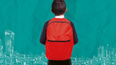 A boy is standing his back to the viewer. He is wearing a red backpack and has dark, short hair.