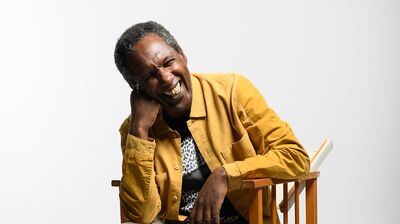 Lemn Sissay wearing a yellow jacket sitting on a chair.