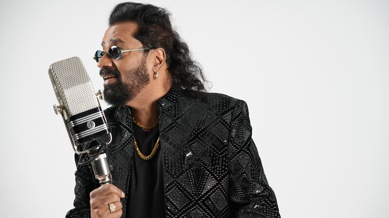 A man wearing sunglasses and a black patterned jacket, holding a large microphone