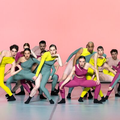 Dancers perform on a stage in colourful costumes posing in crouched positions