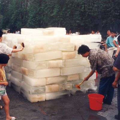 Group of people standing around a large tower of ice blocks, scrubbing them with brushes.