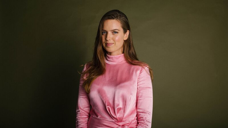 Louise Paley, a young White woman with long brown hair, wearing a long sleeved pink dress