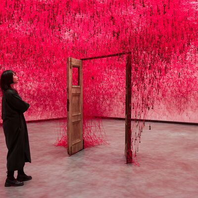 Two people stand on either side of an open door in Chiharu Shiota: Threads of Life