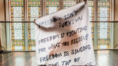 Someone holding up a white sheet with the words 'freedom isn't survival, freedom is fighting for what you believe'