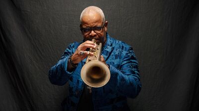 Trumpet player wearing a bright blue suit, playing the trumpet looking to camera