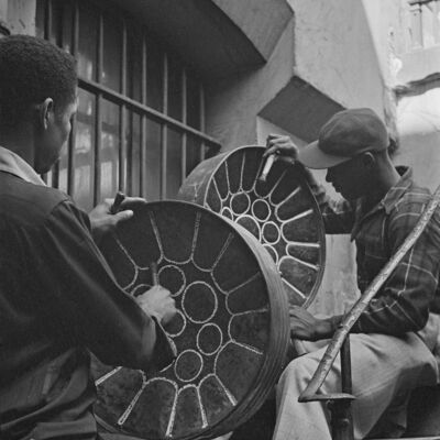 Black and white image of two young men tuning steel pans on a staircase
