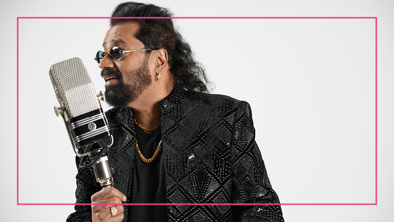 A man wearing sunglasses and a black patterned jacket, holding a large microphone