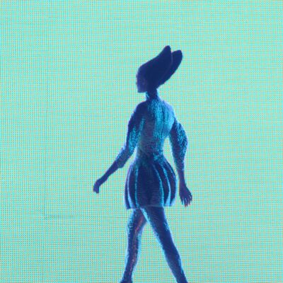 A model wearing a futuristic outfit walking the stage against a green LED screen