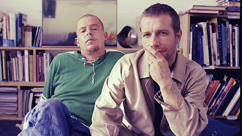 Lee Alexander McQueen and John Gosling sit together in front of a record collection