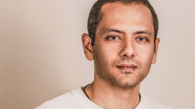 Omar El Akkad wearing a white T shirt against a beige background.