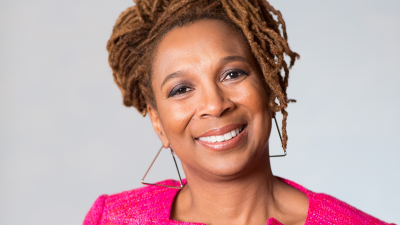 Kimberle Crenshaw wearing a pink blazer against a grey background.