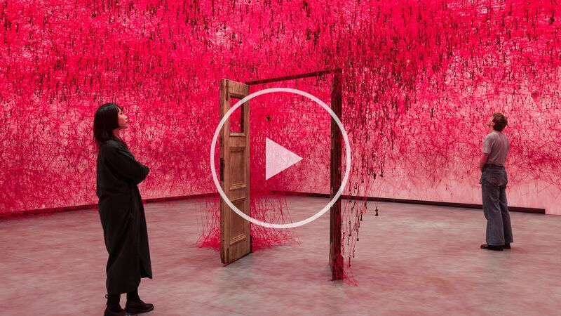 Two people stand on either side of an open door in Chiharu Shiota: Threads of Life