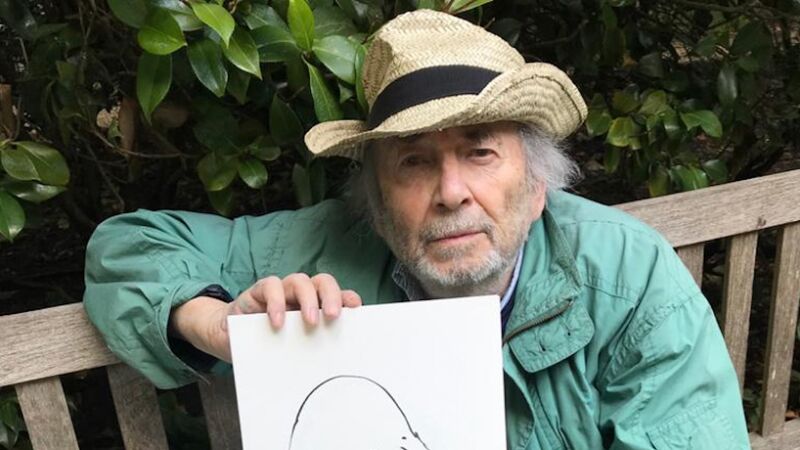 The illustrator and author Quentin Blake; an elderly man wearing a brimmed summer hat. He is sitting on an outdoor bench, holding up one of his illustrations.