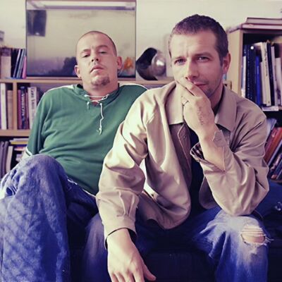 Fashion designer Lee Alexander McQueen and musician John Gosling sitting in the living room of a flat