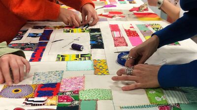 People working on a large fabric patchwork quilt together in a workshop
