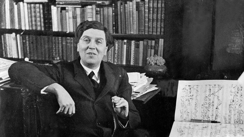 Austrian composer Alban Berg photohgraphed in his workroom in Hietzing. He is seated in a desk chair in front of a full bookcase, an open music manuscript sits on the table in front of him.